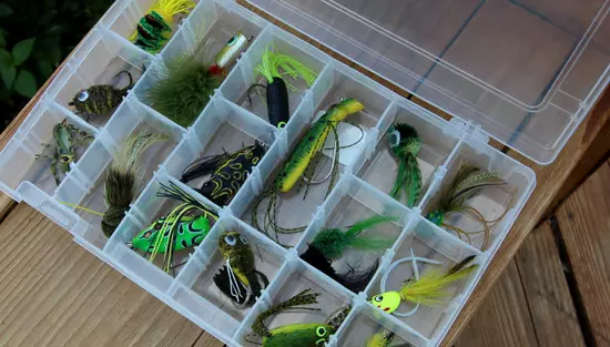 Une boîte en plastique de divers leurres de pêche colorés.